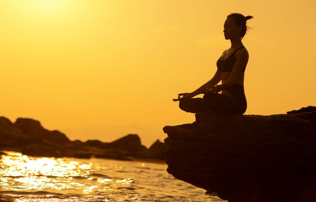 Peaceful person meditating beside a lake at sunrise symbolising healing, clarity, emotional release, and new beginnings.